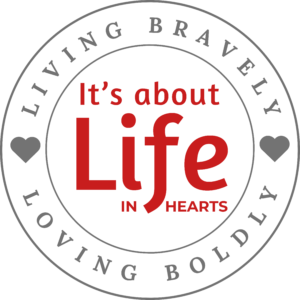 Circular logo with a gray ring and hearts, featuring red text reading 'It's about Life' surrounded by edge lettering.